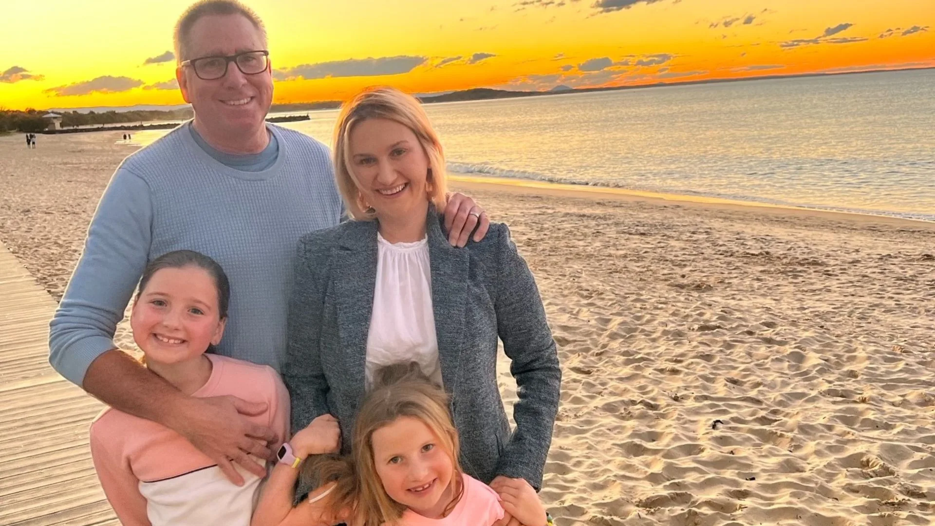 Family posing together on a beach at sunset with the sea and orange sky in the background.