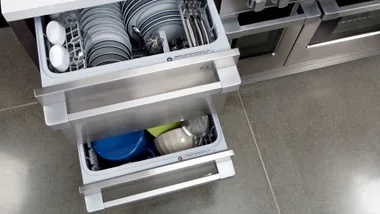 Open double drawer dishwasher with plates and utensils inside.