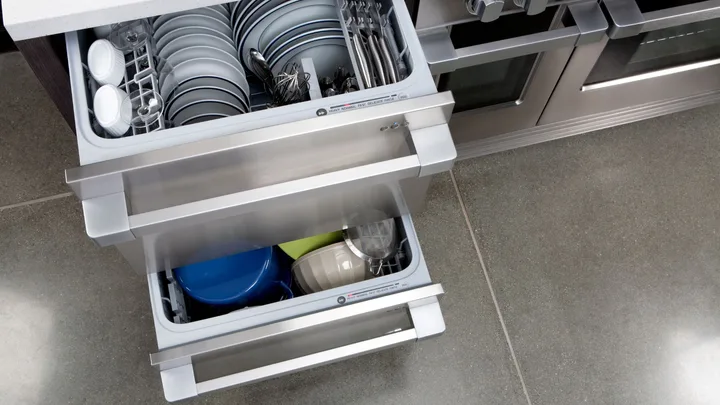 Open double drawer dishwasher with plates and utensils inside.