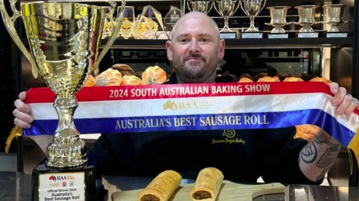 Baker holding a trophy and ribbon for "Australia's Best Sausage Roll" at 2024 South Australian Baking Show.
