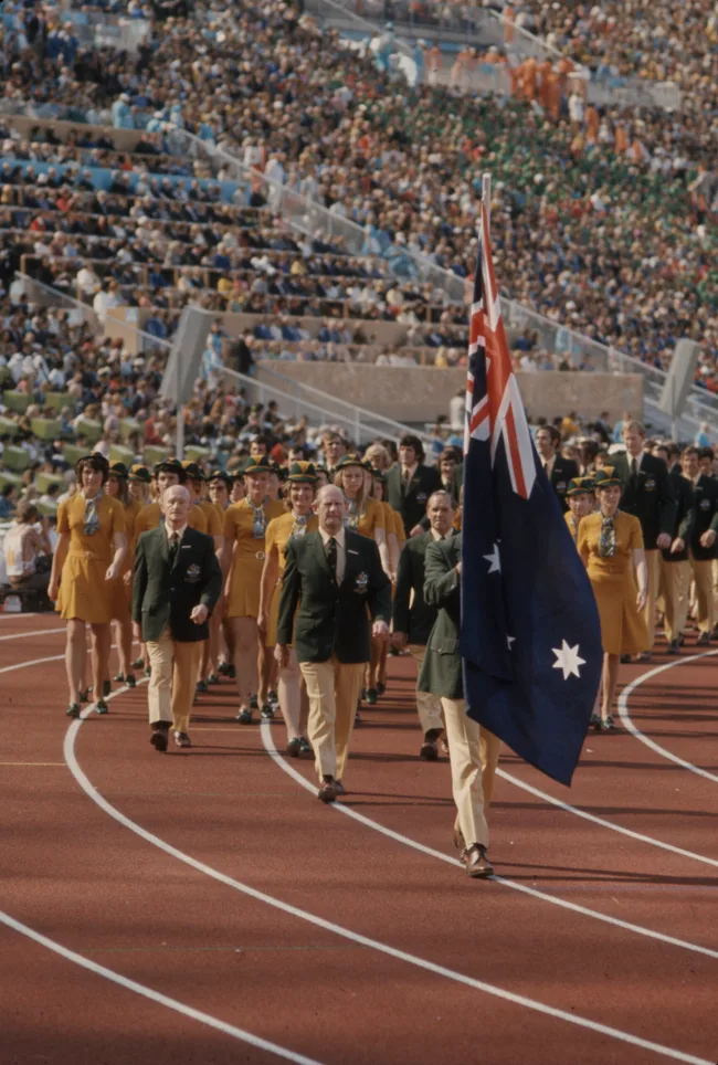 Australian Olympic team marching with flag at a stadium, large crowd in background, 1972 Munich Olympics.
