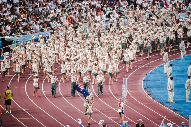 Australian team marching in floral shirts during Sydney 2000 Olympics opening ceremony, waving hats to cheering crowd.