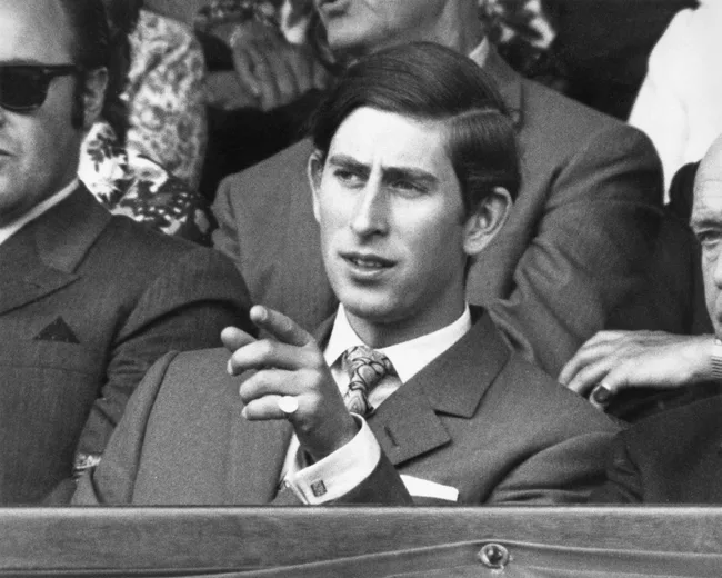 Young man in a suit at a public event, pointing and engaging with companions, black and white photo.