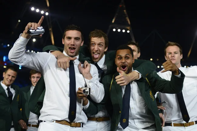 Group of excited men in suits and ties celebrating at a nighttime event, one holding a camera.