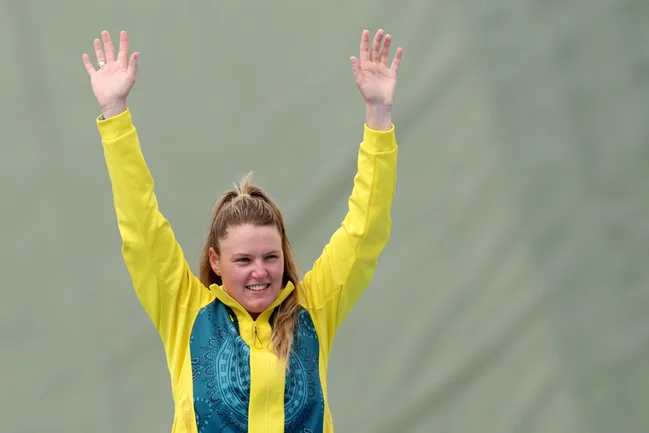Person in yellow and green sports attire raises arms, smiling against a neutral background.