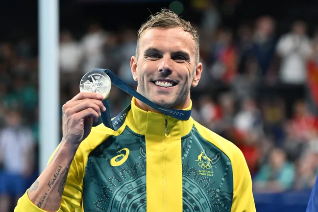 Olympian in Australian tracksuit holding a silver medal with "Paris 2024" lanyard, smiling at the camera.