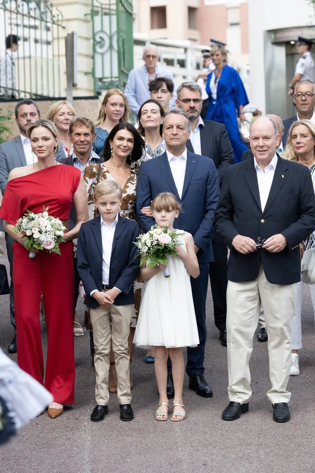 Group photo of people, including a woman in a red outfit holding flowers, beside a man in a blazer, outdoors.