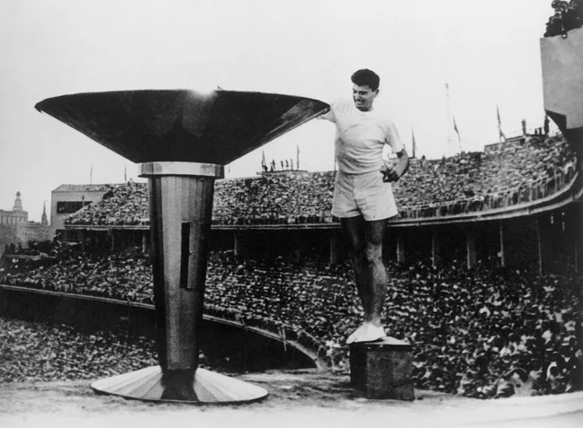 Athlete lighting the Olympic cauldron at a stadium filled with spectators during the 1956 Olympics.