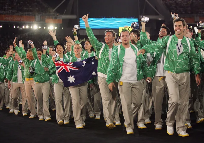 Australian athletes in green jackets celebrate at Athens 2004, one holding the national flag.