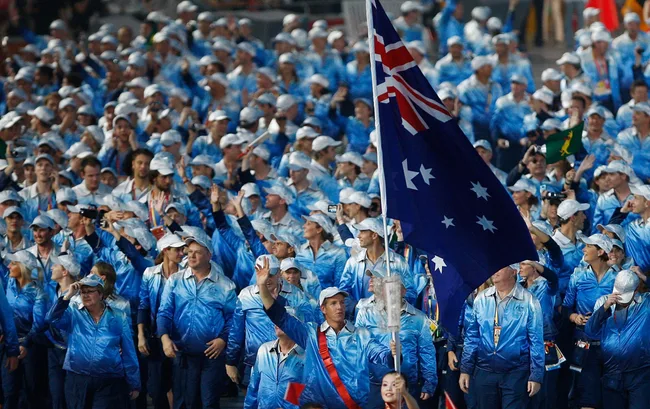 Australian Olympic team in blue outfits, waving flags at an Olympic ceremony.