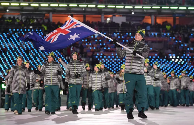 Australian athletes in uniform march at an Olympic opening ceremony; one carries the national flag.