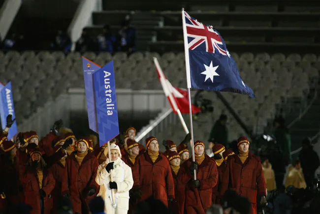 Australian team in red coats marching at the 2002 Winter Olympics, carrying the national flag and a sign.