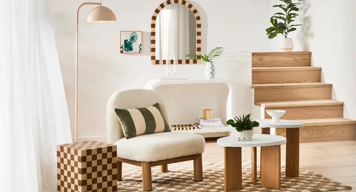 Cozy modern living room with a white chair, checkered table, plants, wood steps, and arched mirror against a white wall.
