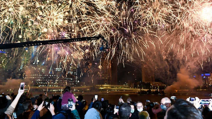 Crowd watching vibrant fireworks display over a city skyline at night.