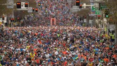 Huge crowd of runners participating in a city marathon, wearing colorful athletic gear, with traffic lights overhead.