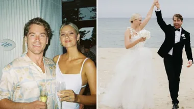 A couple celebrates with champagne; they walk on a beach in wedding attire.