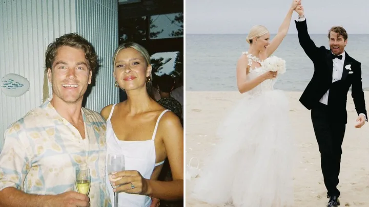 A couple celebrates with champagne; they walk on a beach in wedding attire.