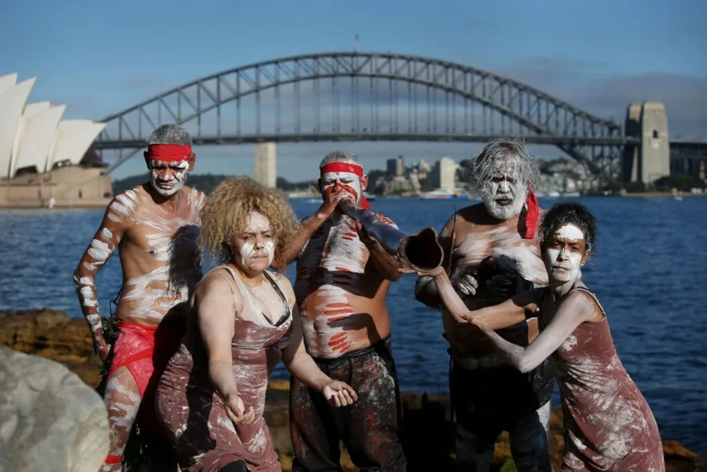 Koomurri Dance Group members pose for photos during a NAIDOC Week event with the Sydney Opera House and Sydney Harbour Bridge in the background.