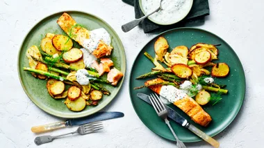Plates with roasted salmon, asparagus, and potatoes, topped with creamy dill sauce.