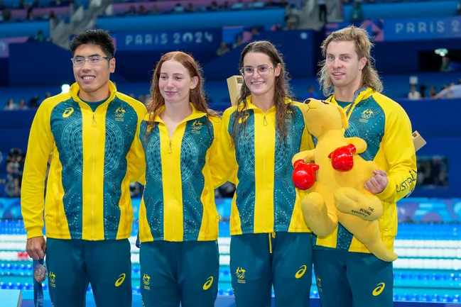 Australian swimmers in team uniforms with medals at Paris 2024, one holding a plush kangaroo.