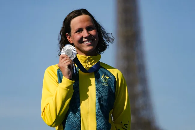 Australian athlete in a yellow jacket smiling and holding a silver medal with the Eiffel Tower blurred in the background.