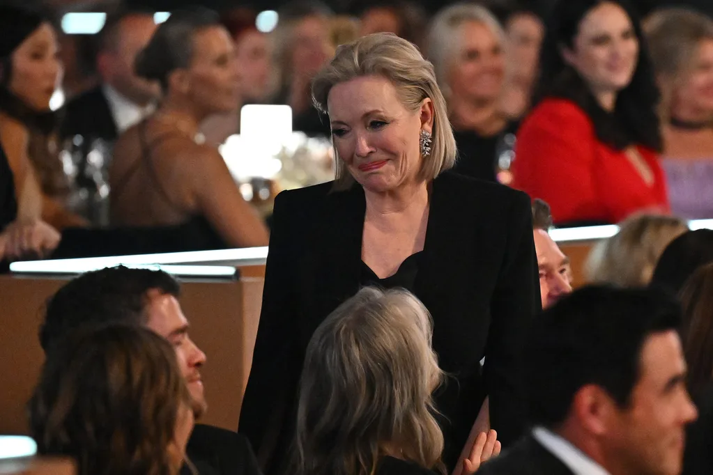 A person in formal attire standing among seated guests at an event, with a warm expression.