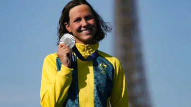 Smiling athlete in yellow jacket holding silver medal, Eiffel Tower in background.