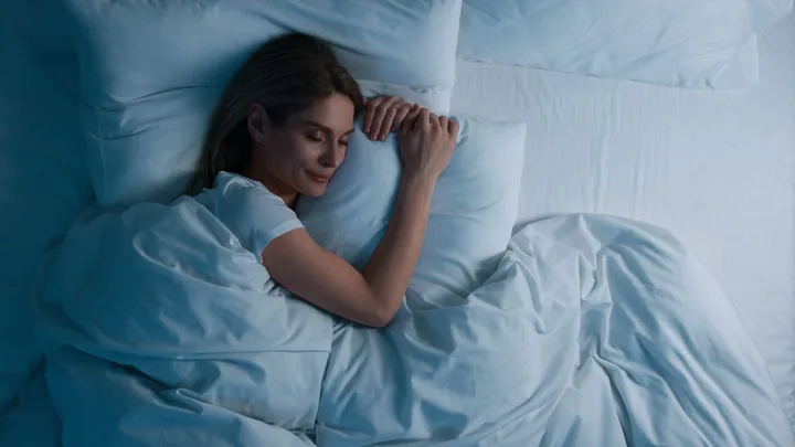A woman peacefully sleeping on a white bed, wrapped in a white blanket, with a serene expression.