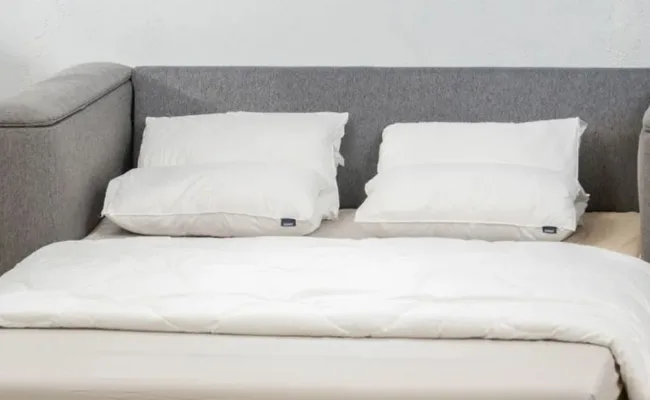 A neatly made bed with a grey headboard, two white pillows, and a white duvet.