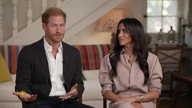 Two people seated on a sofa in a living room, engaged in an interview.