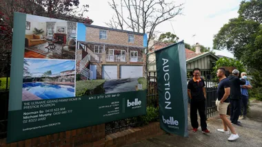 Auction sign for a grand family home with people gathered outside in a residential area.