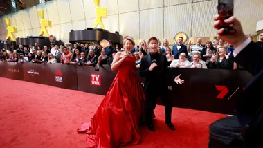 Red carpet event with two excited people posing, crowd cheering in the background.