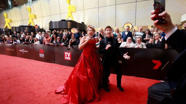 Red carpet event with two excited people posing, crowd cheering in the background.