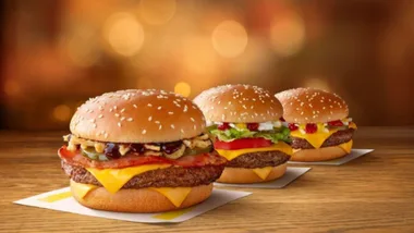 Three cheeseburgers with various toppings on a wooden table against a blurred warm background.