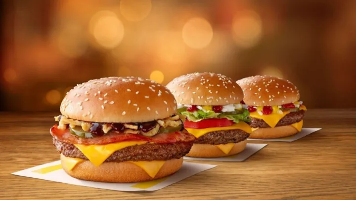 Three cheeseburgers with various toppings on a wooden table against a blurred warm background.