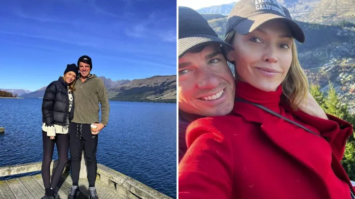 Couple smiling by a scenic lake and mountains, wearing winter clothing.