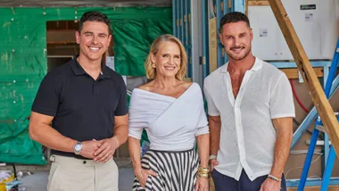 Three people smiling at a construction site, a man in a black shirt on the left, a woman in the center, and a man in white on the right.