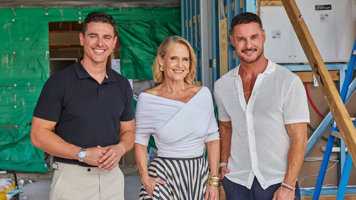 Three people smiling at a construction site, a man in a black shirt on the left, a woman in the center, and a man in white on the right.