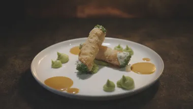Cream cannoli with green garnish and orange sauce on a white plate, artfully arranged with sauce and puree dollops.