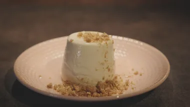 Creamy dessert on a plate, topped and surrounded by crumbled brown biscuit pieces.