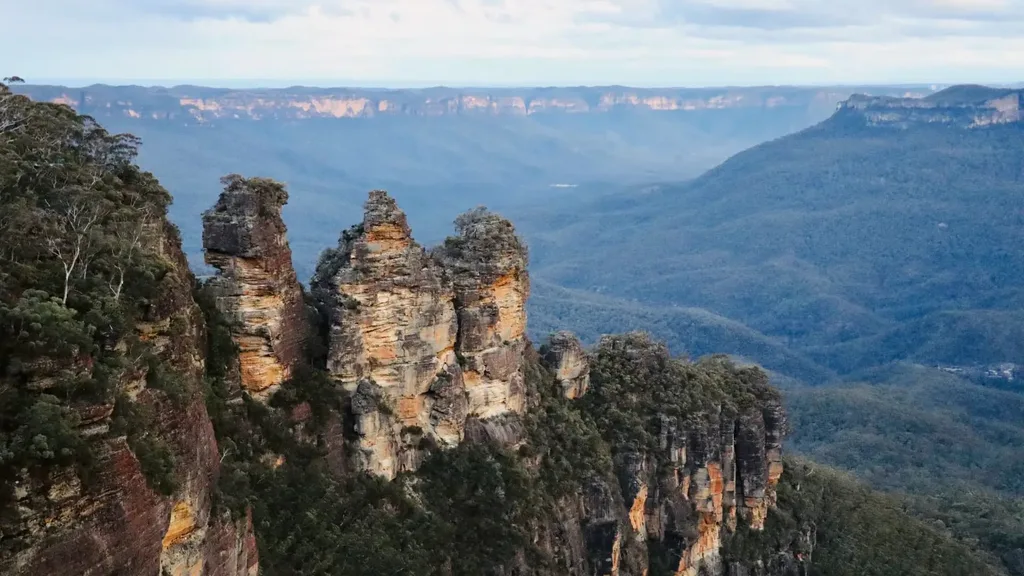 The Three Sisters rock formation in Australia's Blue Mountains under a cloudy sky.