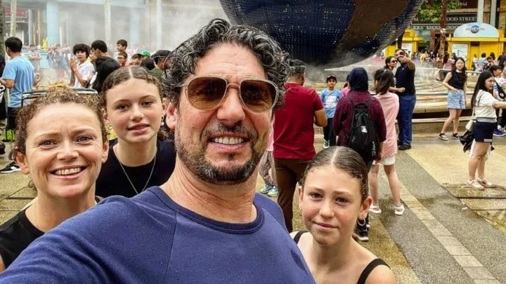 "Group selfie of a family in front of a fountain with a globe sculpture, surrounded by a lively crowd."