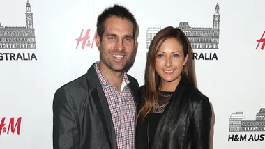 A smiling couple poses in front of an H&M Australia backdrop at an event.