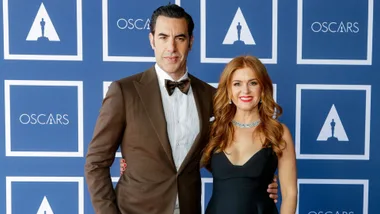 A couple posing in formal attire at an Oscars-themed event with a blue and white backdrop.
