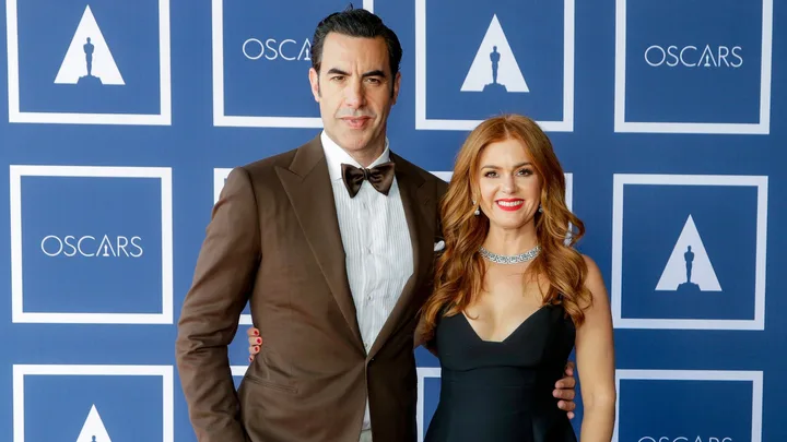 A couple posing in formal attire at an Oscars-themed event with a blue and white backdrop.