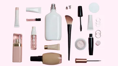 Various makeup and beauty products arranged on a light pink background.