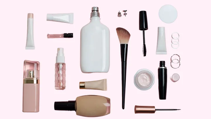 Various makeup and beauty products arranged on a light pink background.