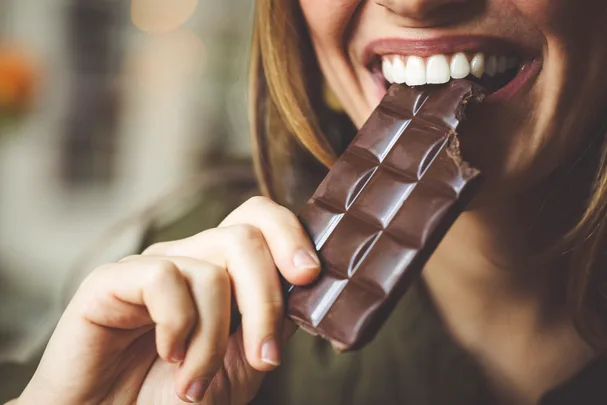 Close up of woman eating a bar of dark chocolate.