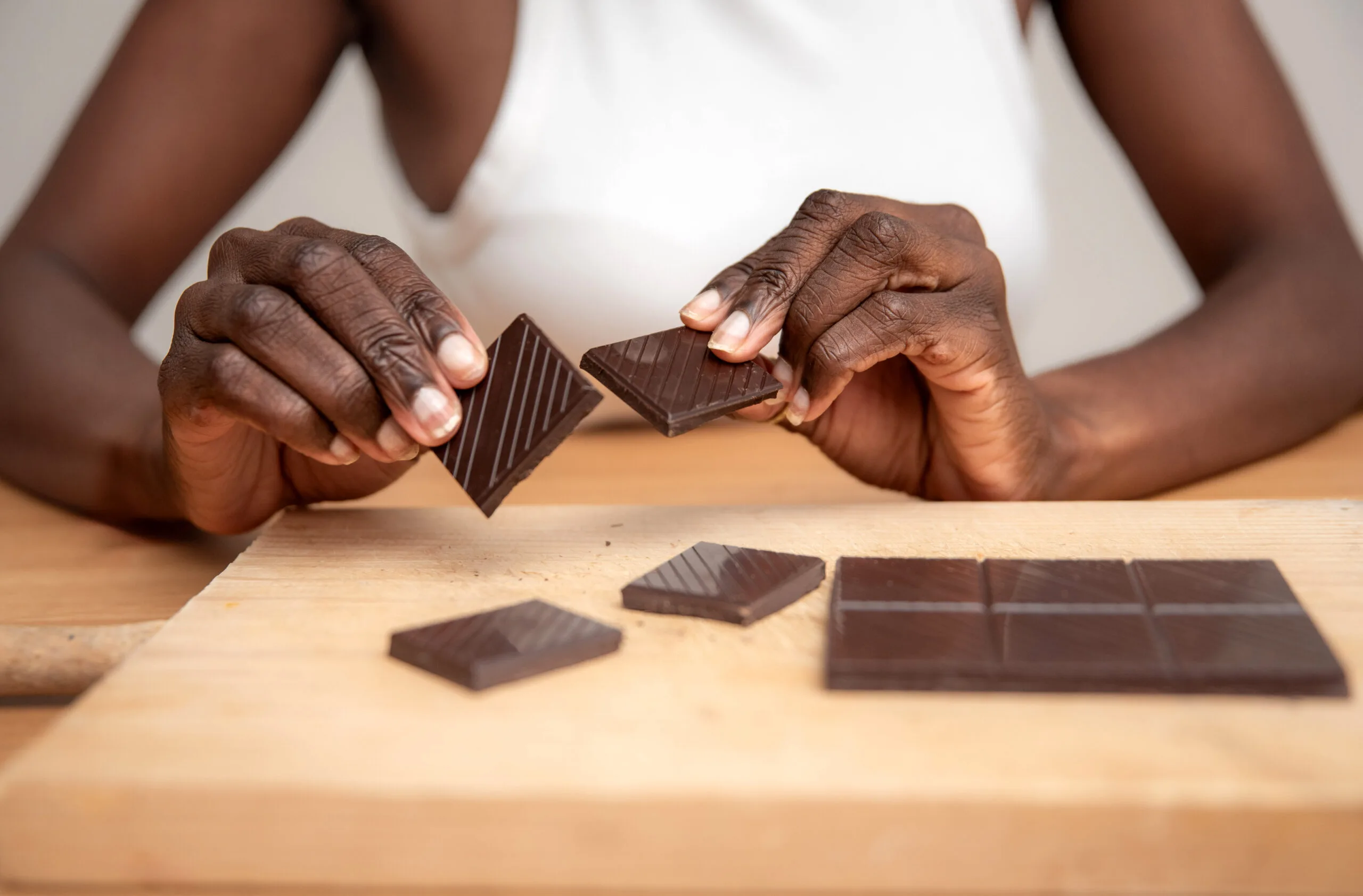 A woman breaking apart a bar of dark chocolate.
