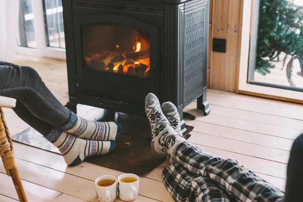 people at home dressed in winter clothes warming up by a fireplace